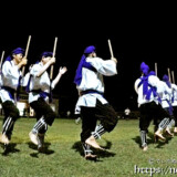 棒を手に行進する演者たち-野原マストリャー